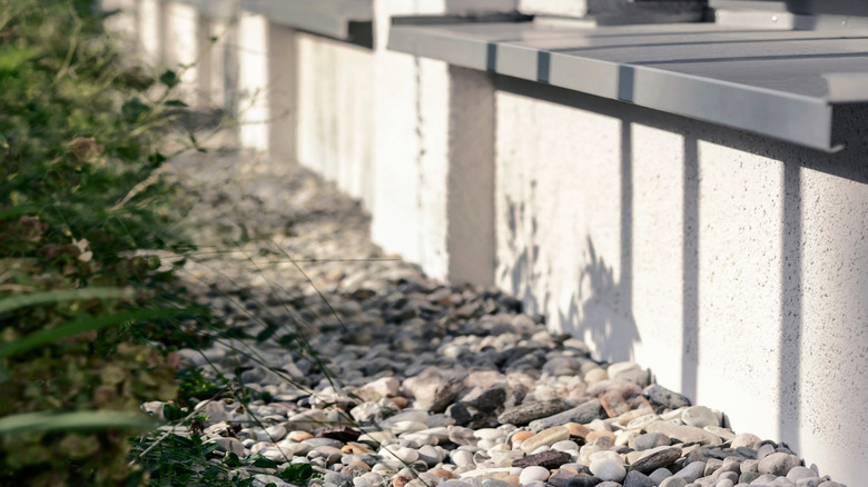 A French drain around the perimeter of a house is covered in gravel