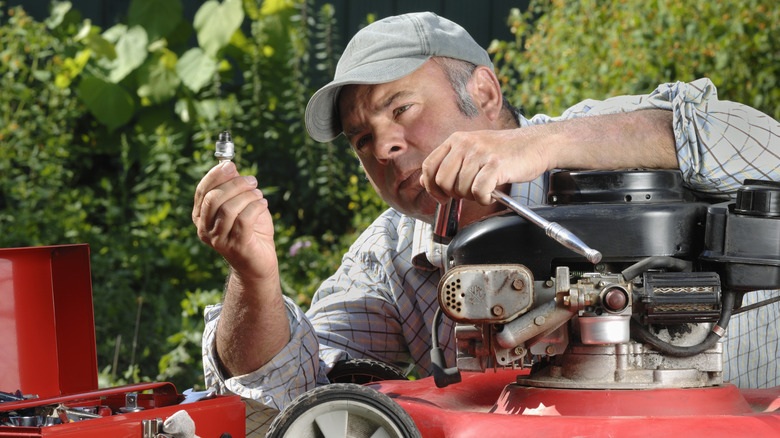 A man changing the spark plug on a lawn mower