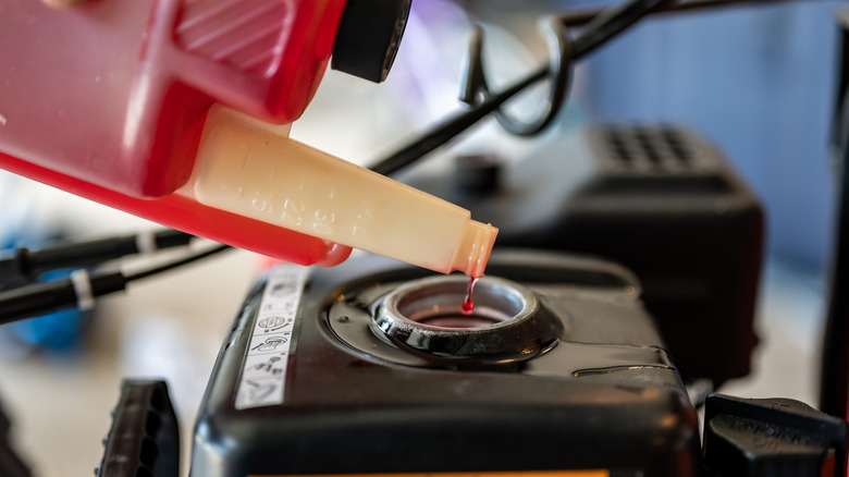 A person adding fuel stabilizer to a lawn mower gas tank