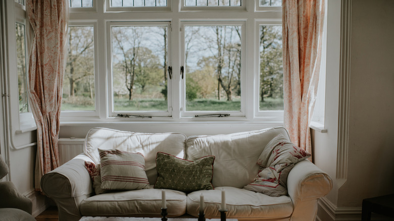a couch and bay windows with opened floor length curtains