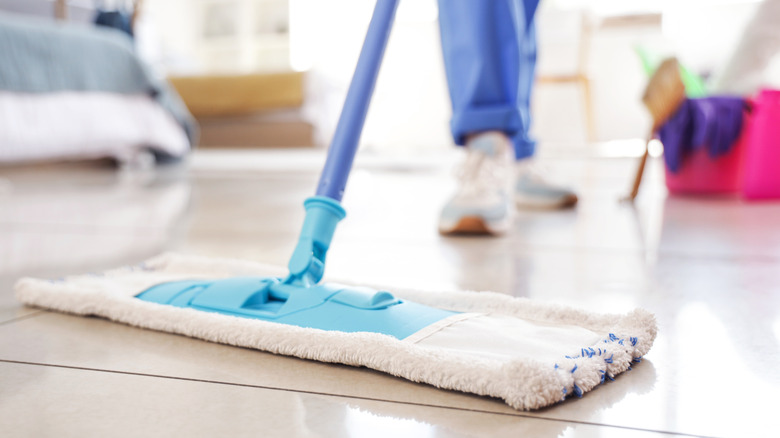 A person using a flat microfiber mop on a light-colored tiled floor