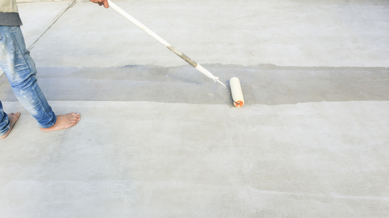 A person uses a roller brush to apply sealant to a concrete patio