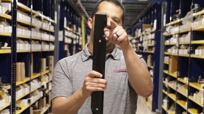 A person holding a new mower blade in a store while standing in front of several shelves of parts