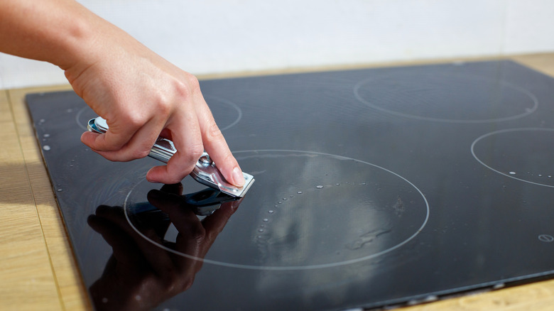 Person using razor blade to clean stains off glass stovetop