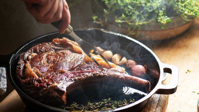 A person using a cast iron skillet to prepare meat and vegetables