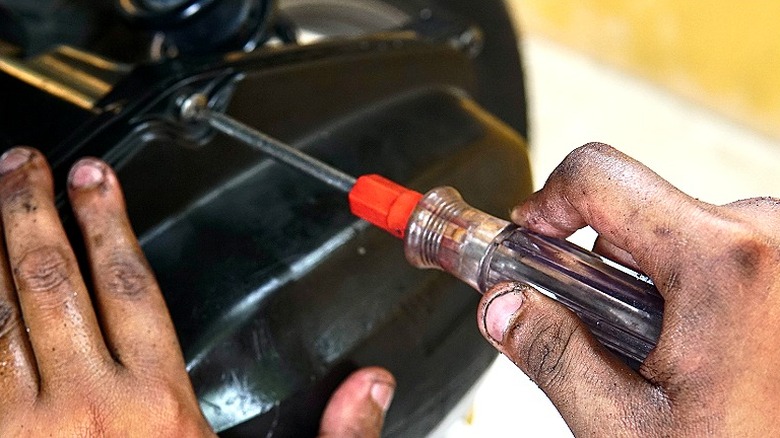 Close-up of a person with hands covered with oil using a screwdriver