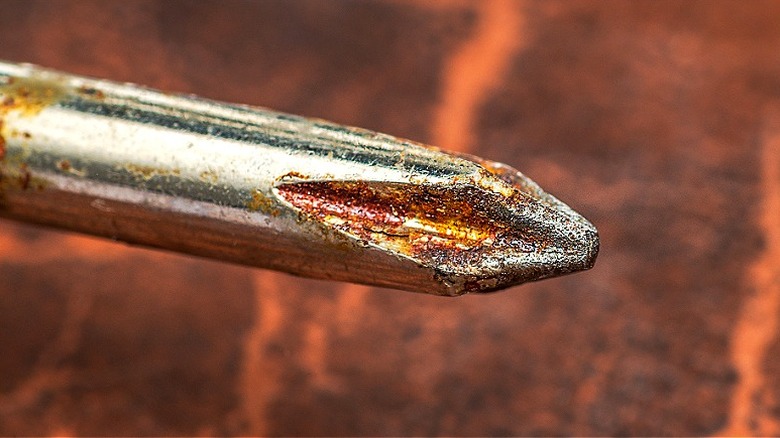 Close-up macro shot of a rusty Phillips head screwdriver tip on a textured background
