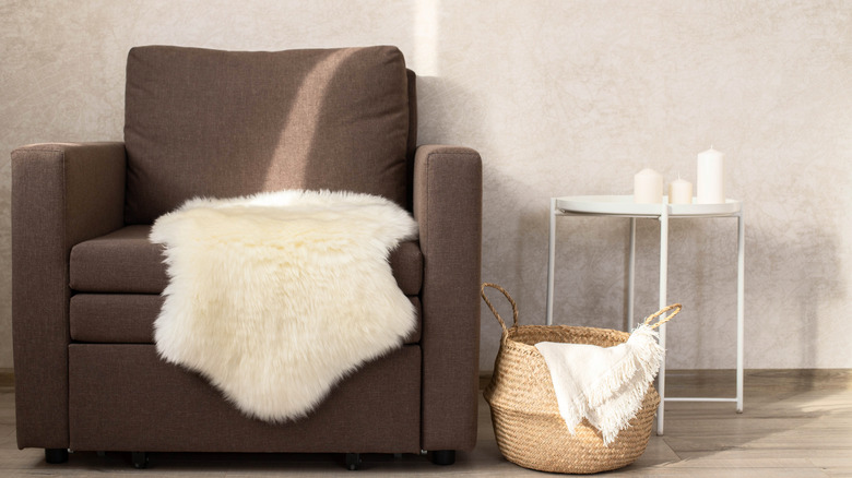 A white sheepskin rug on a cozy brown chair next to a wicker basket