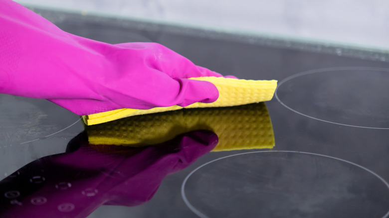 hand in pink glove wiping a black stovetop
