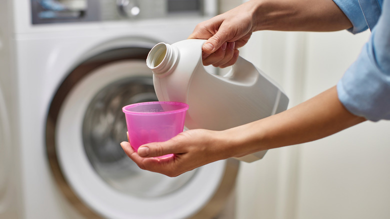 person pouring cleaner into cup for washer