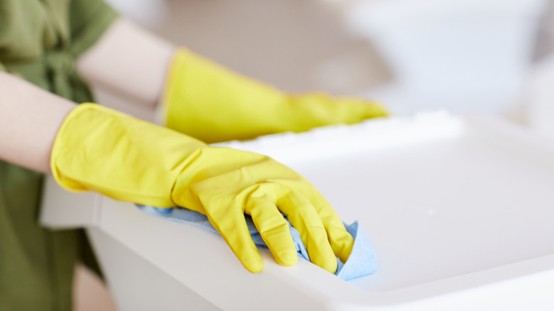 A woman with gloves cleaning out her trash can liner