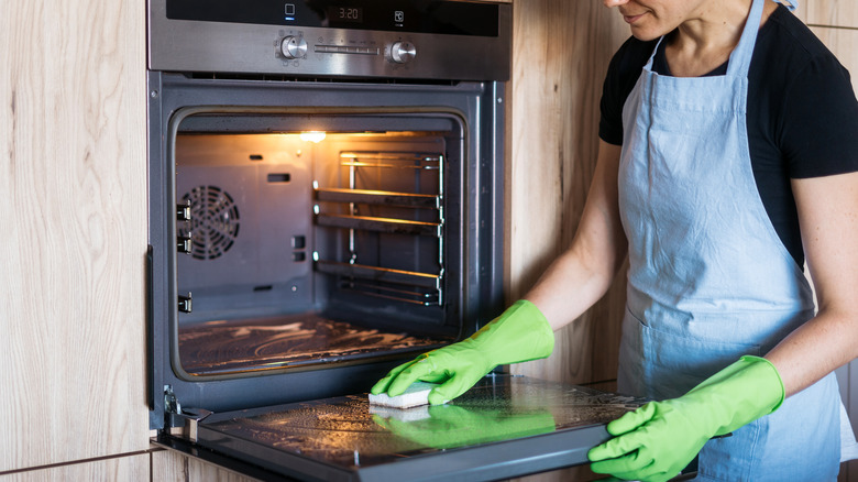 Person wearing gloves cleaning oven with sponge