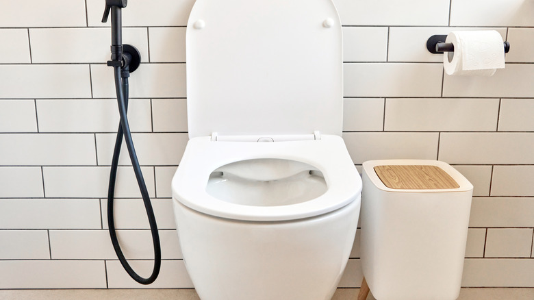 A trash can sitting next to a toilet in a bathroom
