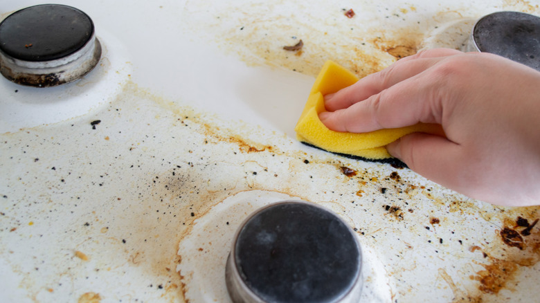 Close-up of person cleaning a stovetop with a sponge
