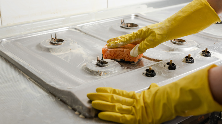 Hands wearing yellow gloves cleaning stovetop