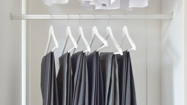 Several pairs of dress pants hanging in a closet