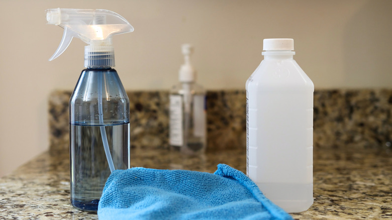 A spray bottle, cloth, and bottle of rubbing alcohol sit on a kitchen counter