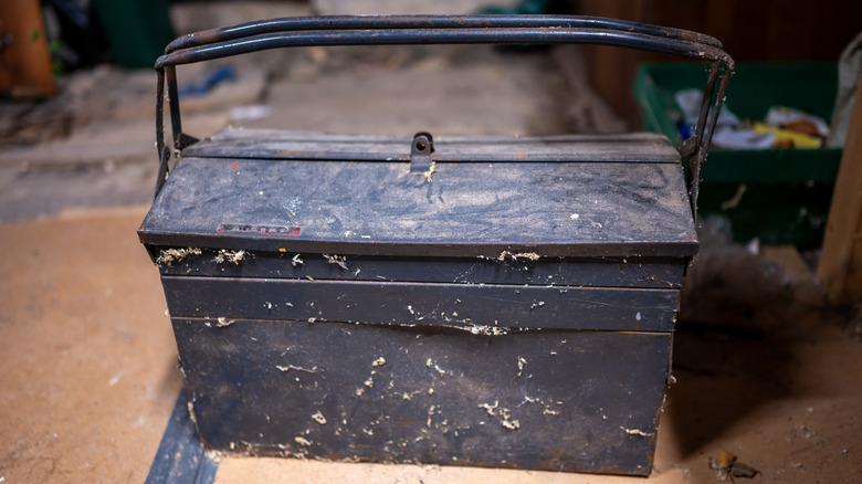 Dirty black metal tool box sits on a tool bench, waiting to be cleaned.