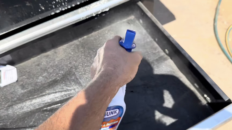 Man sprays down the inside of a dirty tool box with degreaser.
