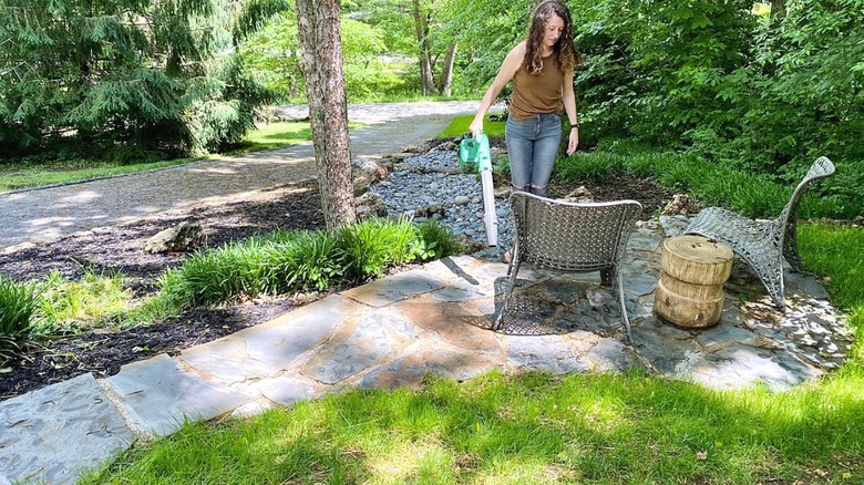 Woman using a hand blower to remove pollen from patio.