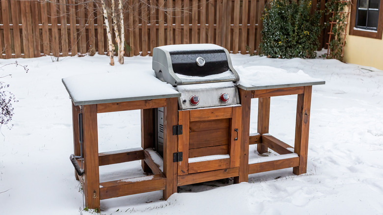 A grill sits in a snowy backyard