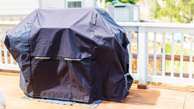 A gas grill, covered with a black grill cover, is stored on the back patio.