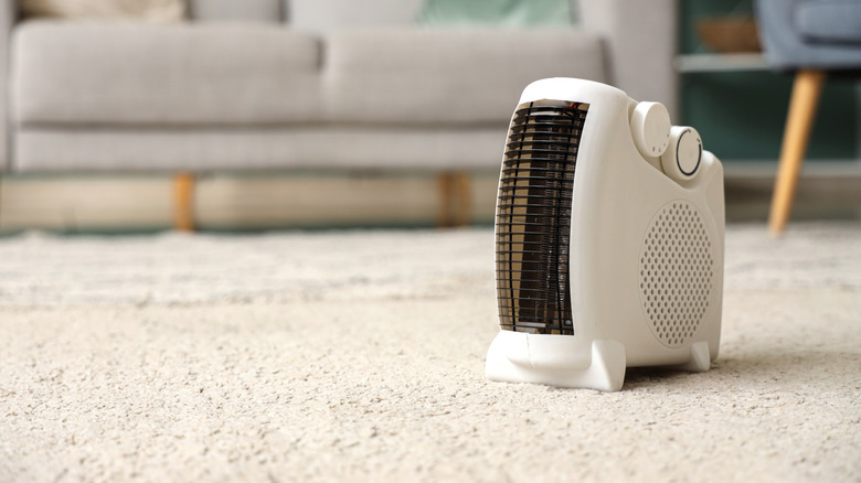 A white electric fan heater on a living room floor.
