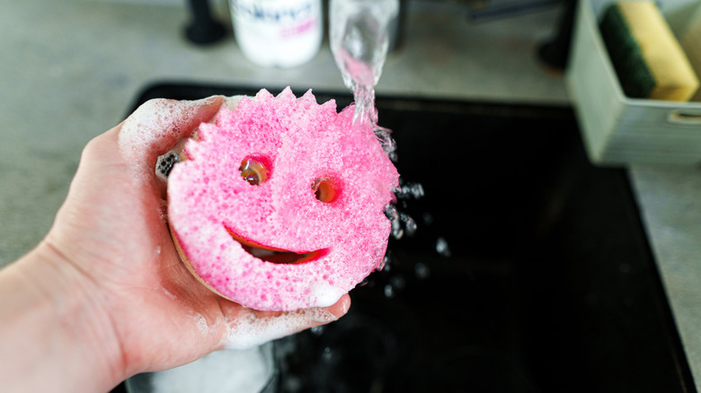 A person holds a sudsy Scrub Mommy sponge over a sink