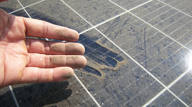 A hand in front of dirty solar panels with finger marks