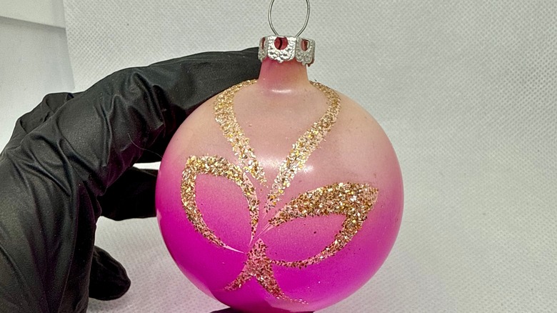 A gloved hand holding a pink vintage ornament
