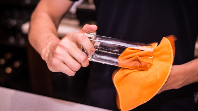 Man's hands drying the inside of a clean glass with an orange cloth.