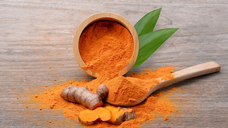 Brightly colored turmeric powder in a wooden bowl spilling onto a wooden surface.
