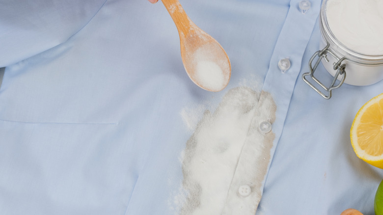 Out-of-frame hand holding a wooden spoon with a DIY stain remover mixture, and letting the mixture soak onto a stained blue shirt.