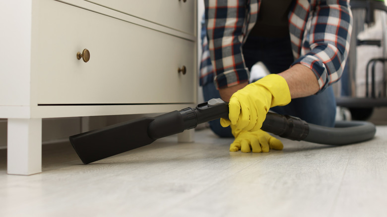Man vaccuming floor under a dresser.