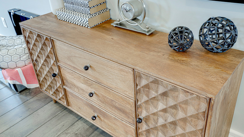 A wooden dresser with a clock, books, and decorative pieces.