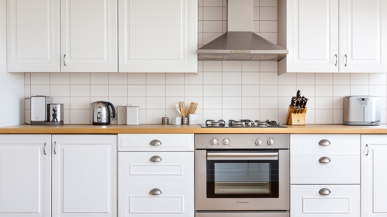 A white kitchen with stainless steel oven and hood, several small appliances on the wooden countertop