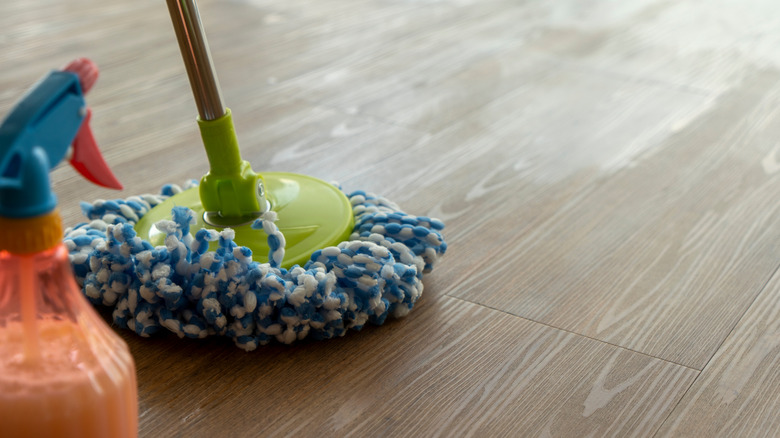 A spray bottle and mop pictured on a vinyl gray wood plank floor