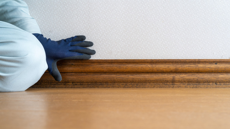 A person checking a wooden baseboard.