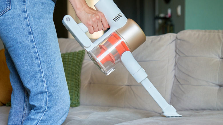 A person vaccuming a sofa