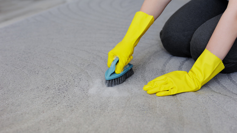 Woman wearing yellow gloves scrubbing carpet
