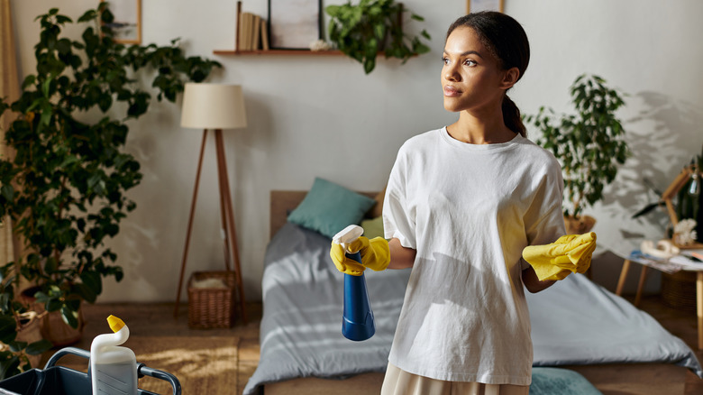 a woman cleaning her bedroom while holding a rag and spray bottle