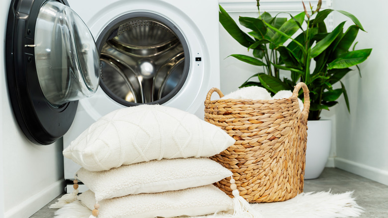 bedding in laundry basket and pillows outside of washing machine