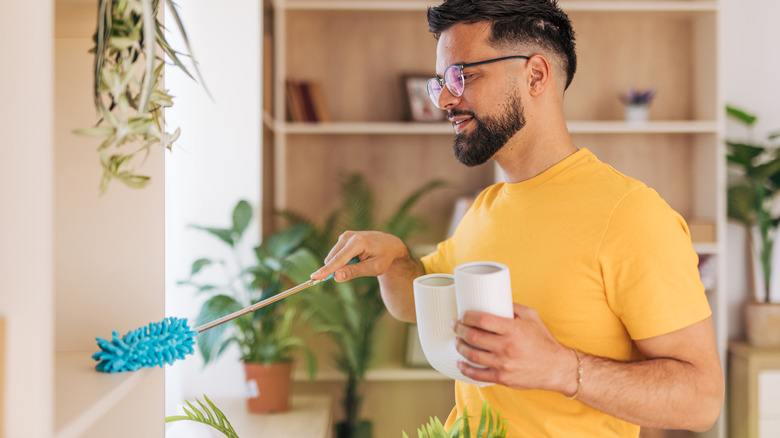 man dusting shelf while holding planter