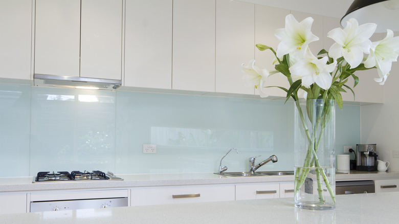 A vase of white flowers in a white kitchen with a glass backsplash