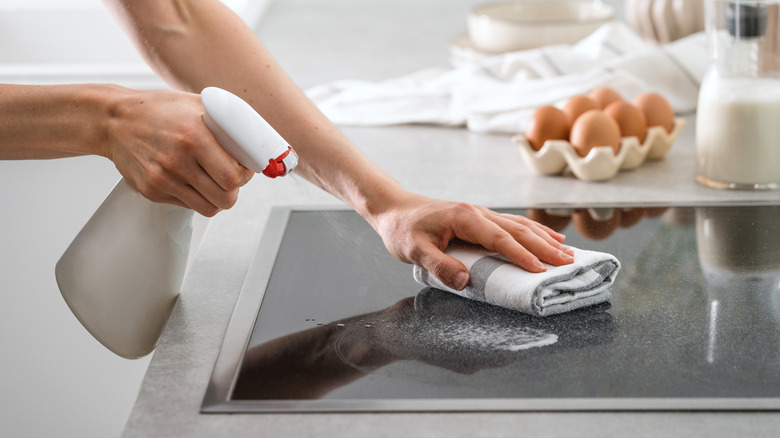 Woman cleaning glass stovetop with spray bottle and rag