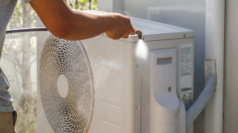 A homeowner washing the exterior of an air conditioning unit using a hose