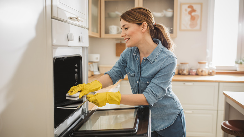 Woman wearing gloves cleaning oven with a sponge