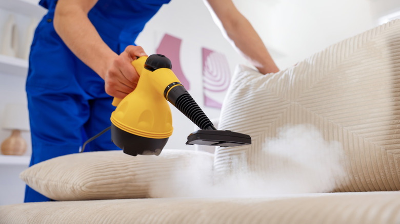 Hand holding yellow steam cleaning tool above couch