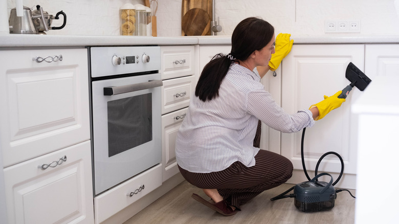 Woman cleaning white cabinets with steam cleaner