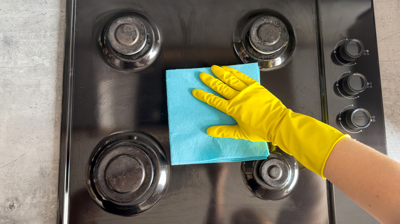 A gloved-hand wiping down a gas stove